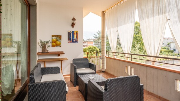 Un balcon agrémenté de meubles en osier, d’une petite table, d’une plante en pot et d’un tableau accroché au mur.