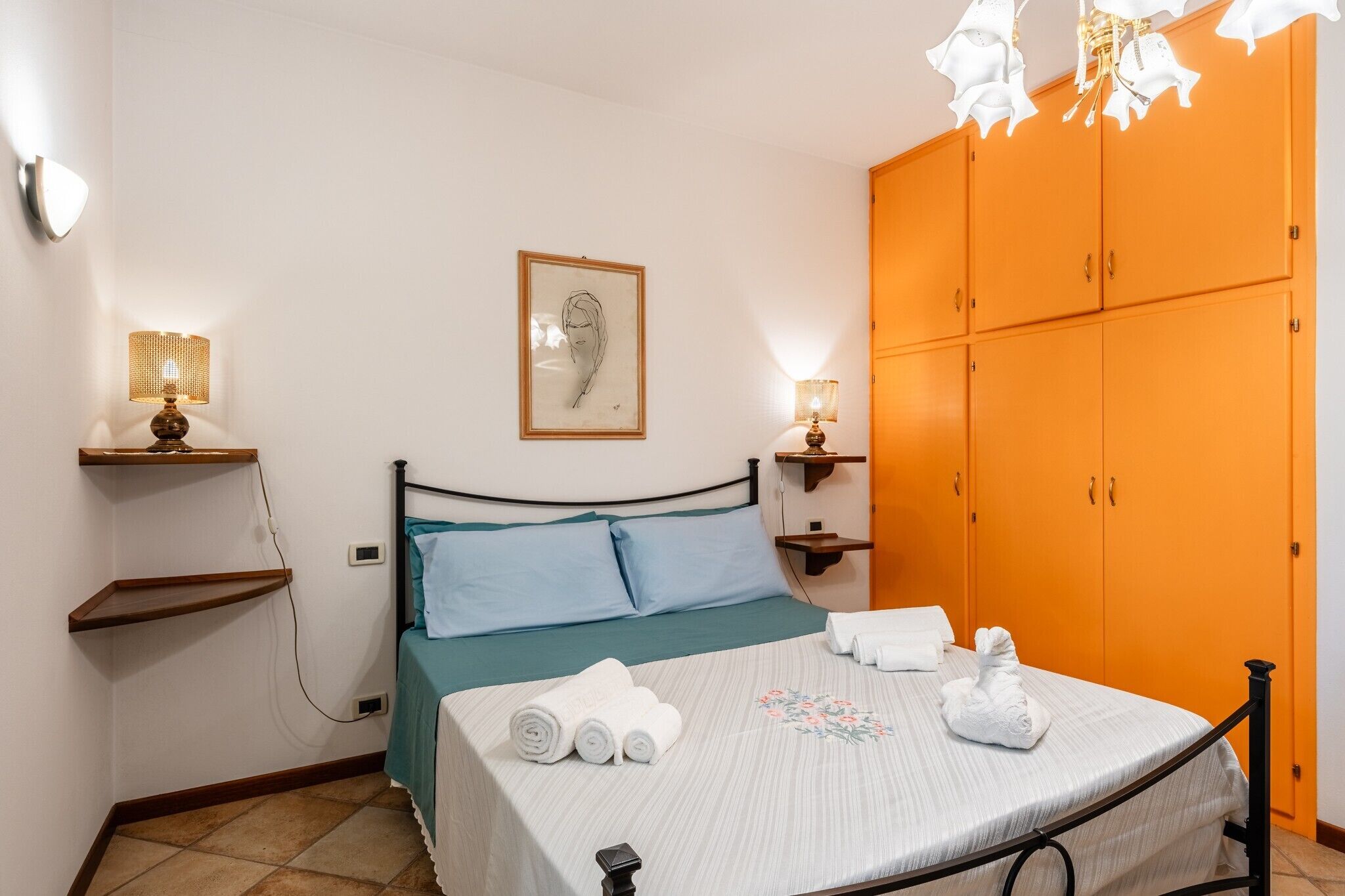 A bedroom with a bed, pillows, a framed picture, a wardrobe, and bedside lamps.