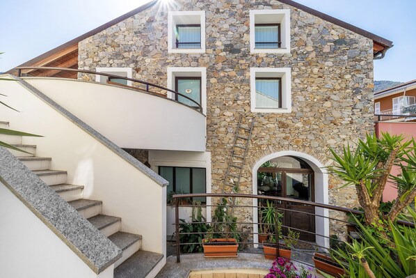A stone building with a staircase, multiple windows, and potted plants.