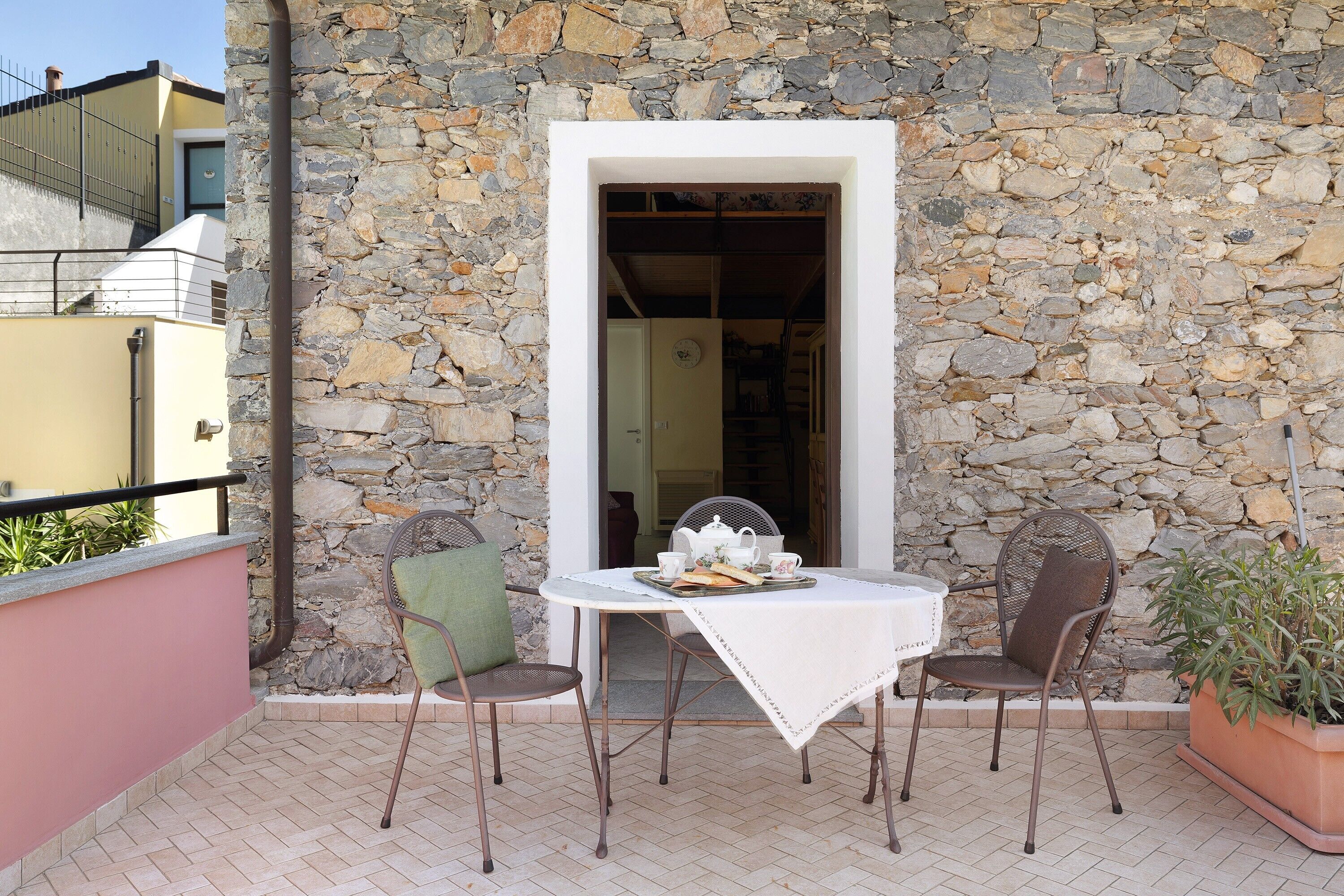 Un mur de pierre, une porte blanche, une table avec des chaises et une plante en pot.