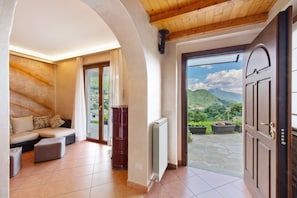Ein Zimmer mit Holzboden, einer Couch, einem Heizkörper und einer Tür zu einem Balkon mit Bergblick.