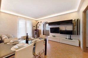 Zona pranzo moderna con tavolo imbandito per quattro persone, divano e televisore a parete.