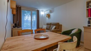 Ruokailutila, jossa on puinen pöytä, tuoleja, vihreä nojatuoli, sohva ja ikkuna, jossa on verhot.