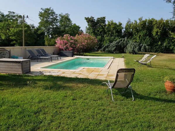A backyard with a swimming pool, lounge chairs, and a grassy area.