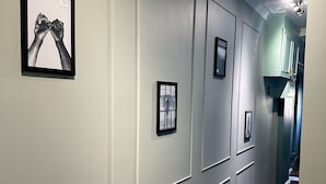 A hallway with framed artwork on the walls, a CCTV warning sign, and a door leading to a room with teal cabinets. - Guest&Rest Hotel (London)