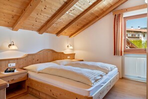 Une chambre avec un plafond en bois, un lit avec une literie blanche, deux lampes de chevet, une table de chevet et une fenêtre avec des rideaux.