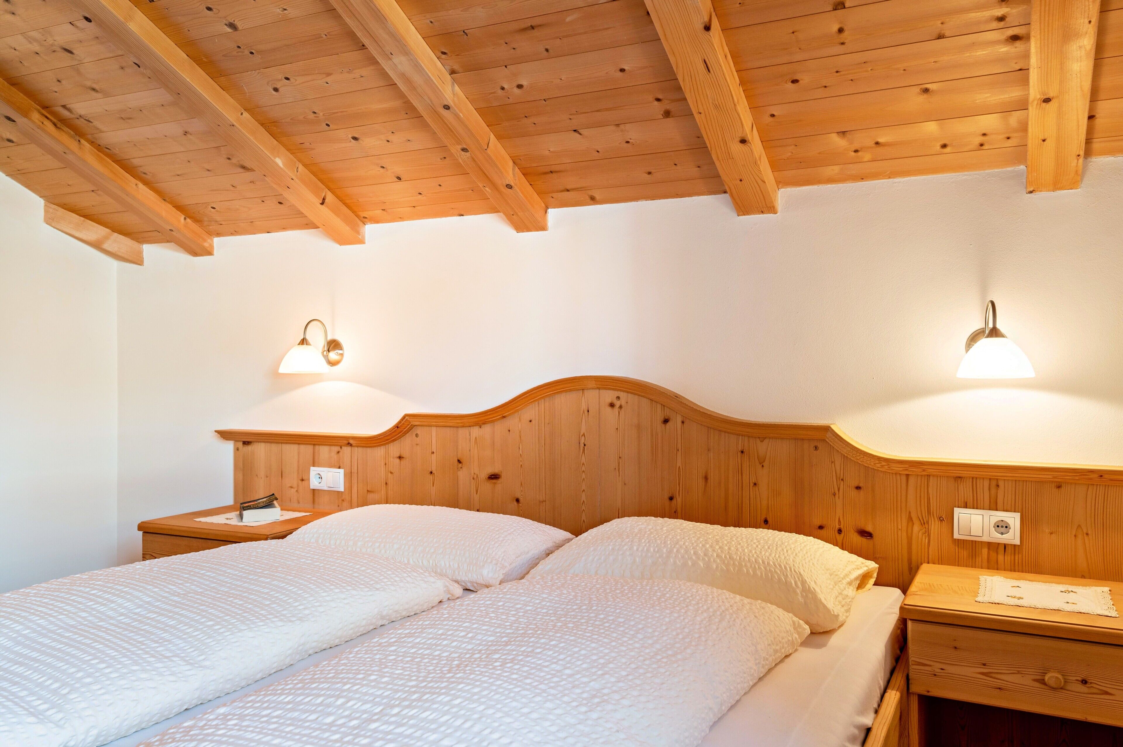 Una habitación con estructura de madera, una cama, dos mesitas de noche y lámparas de pared.