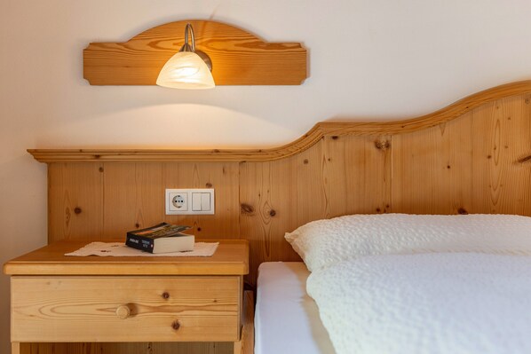 Une tête de lit en bois avec une lampe, une table de chevet avec un livre et une boîte de mouchoirs, et un lit blanc avec une couverture à motifs.