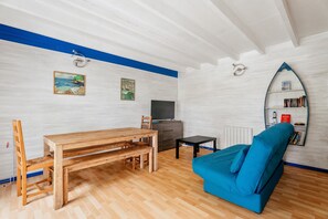 Ein Zimmer mit einem Holzespeisetisch, einem blauen Sofa, einem Fernseher und einem Bücherregal.