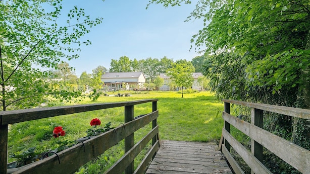 A wooden bridge leading to a grassy area with a house in the background.