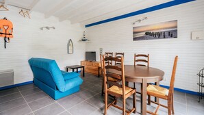 A room with a dining table, chairs, a blue sofa, a TV, and a painting of a sunset.