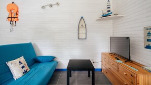 A room with a blue sofa, a small black table, a wooden dresser with a TV, and a surfboard decoration on the wall.