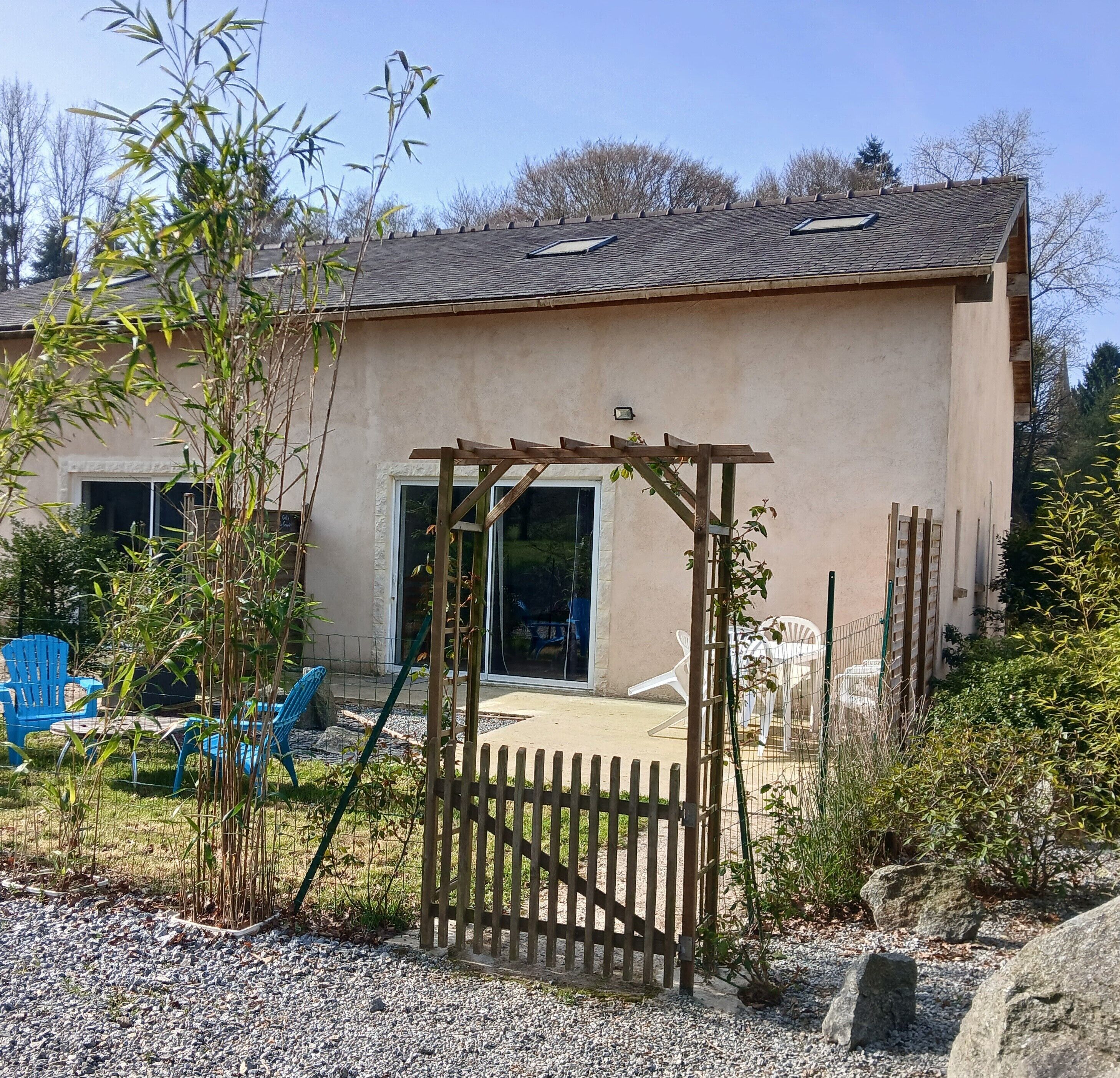 Ein Haus mit einer Holzpergola, einem Schotterweg und einem durch eine Zäheingefassten Garten.