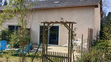 Ein Haus mit einer Holzpergola, einem Schotterweg und einem durch eine Zäheingefassten Garten.