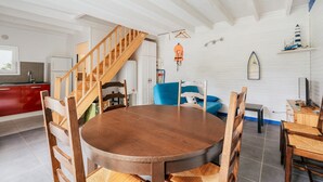 A dining area with a round wooden table, chairs, a staircase, and a kitchen in the background.