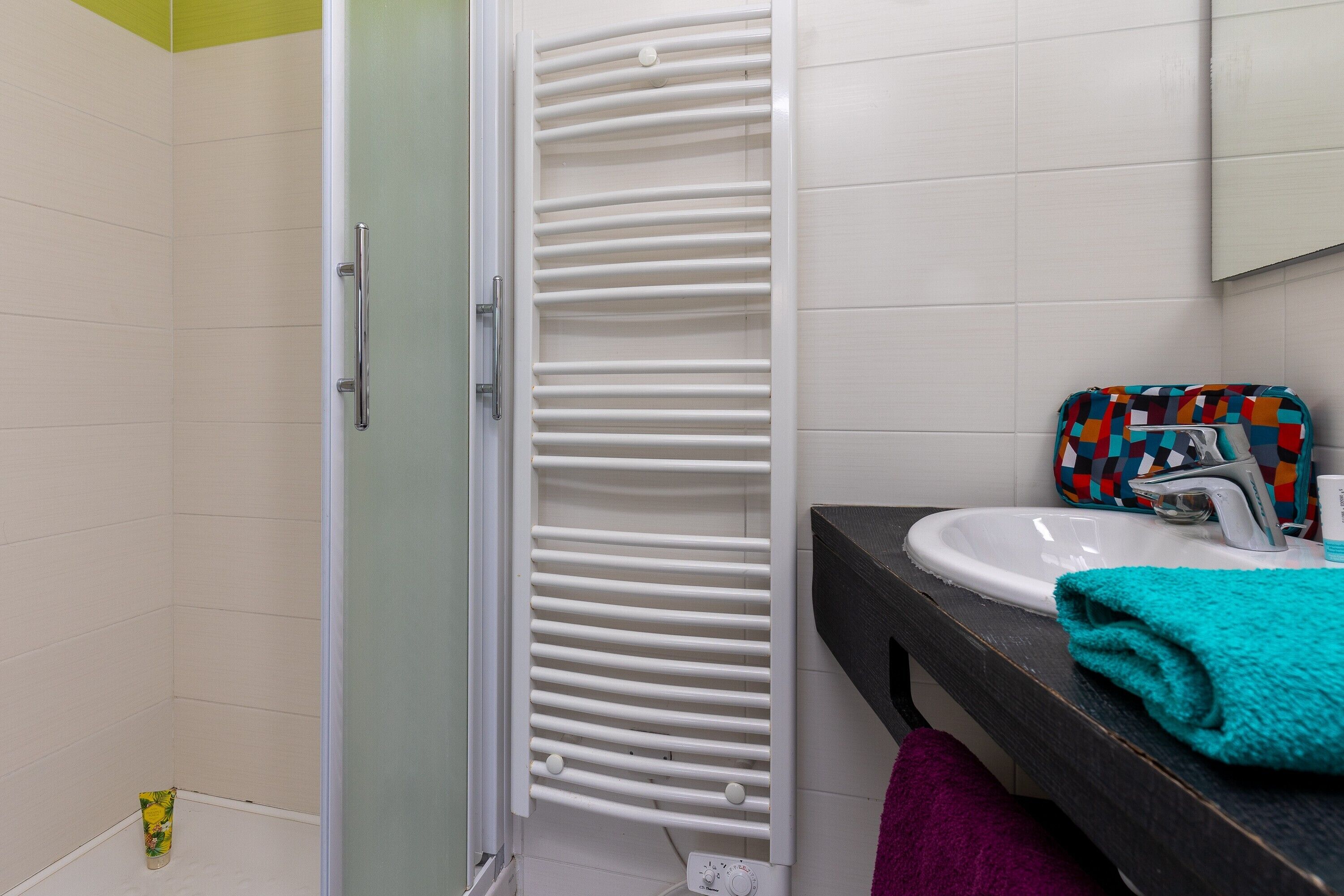A bathroom with a white radiator, a sink with a faucet, a towel, and a colorful bag on the counter.