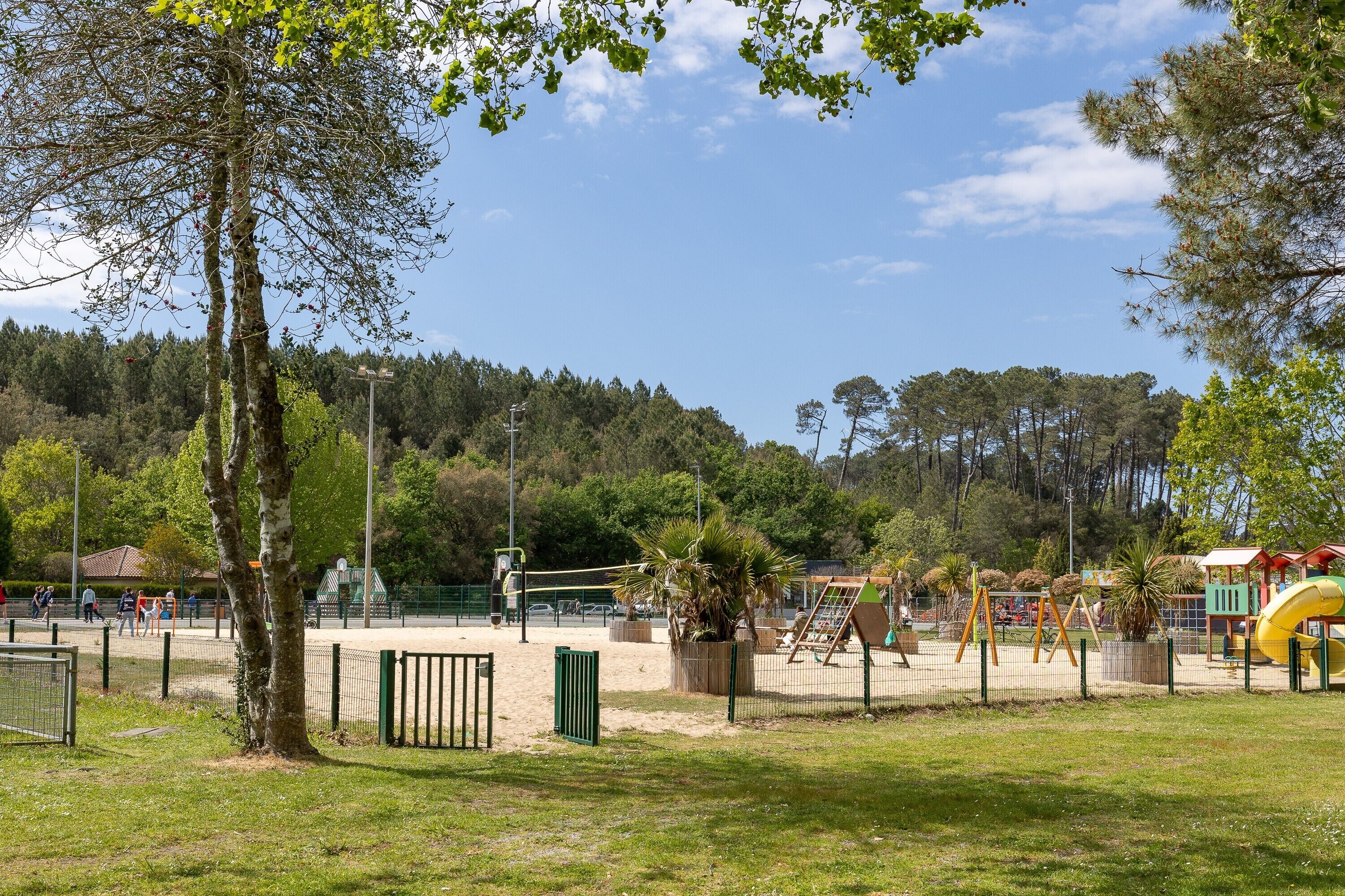 A park with playground equipment, a fenced area, and trees.