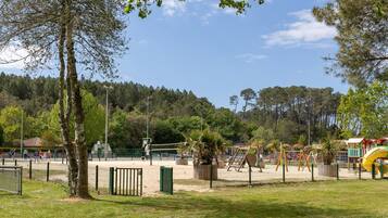 A park with playground equipment, a fenced area, and trees.