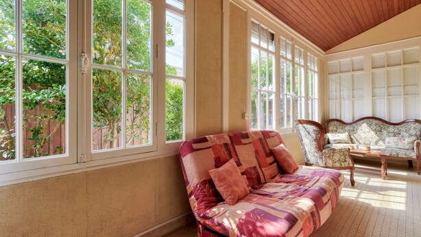 A sunlit room with large windows, a patterned sofa, and a floral armchair.