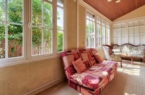 A sunlit room with large windows, a patterned sofa, and a floral armchair.