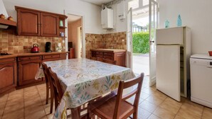 A kitchen with wooden cabinets, a dining table with a floral tablecloth, a coffee maker, and a refrigerator.