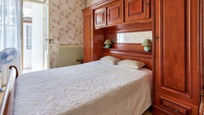 A bedroom with a bed, wooden wardrobe, and a radiator.