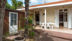 A building with a wooden exterior, a covered patio with white chairs, and a door leading to an interior space.