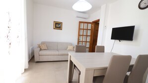 Ein Wohnzimmer mit einer Couch, einem Esstisch mit Stühlen, einem an der Wand befestigten Flachbildfernseher und einer Glastür.