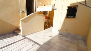 Eine geflieste Terrasse mit Treppe, einem kleinen Fenster und einer Tür zu einem Innenraum.