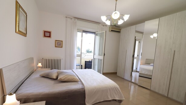 Ein Schlafzimmer mit einem Bett, Nachttischlampen, einer Heizung, einer Deckenleuchte und einer Schiebetür, die auf einen Balkon führt.