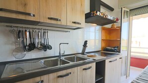 Een moderne keuken met houten kastjes, een roestvrijstalen spoelbak en diverse keukengerei dat aan de muur hangt.