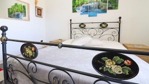 Een slaapkamer met een bed met metalen frame, witte beddengoed en drie ingelijste foto's aan de muur.