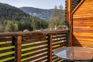 Un balcon en bois avec une table en métal et une vue sur une chaîne de montagnes boisées.
