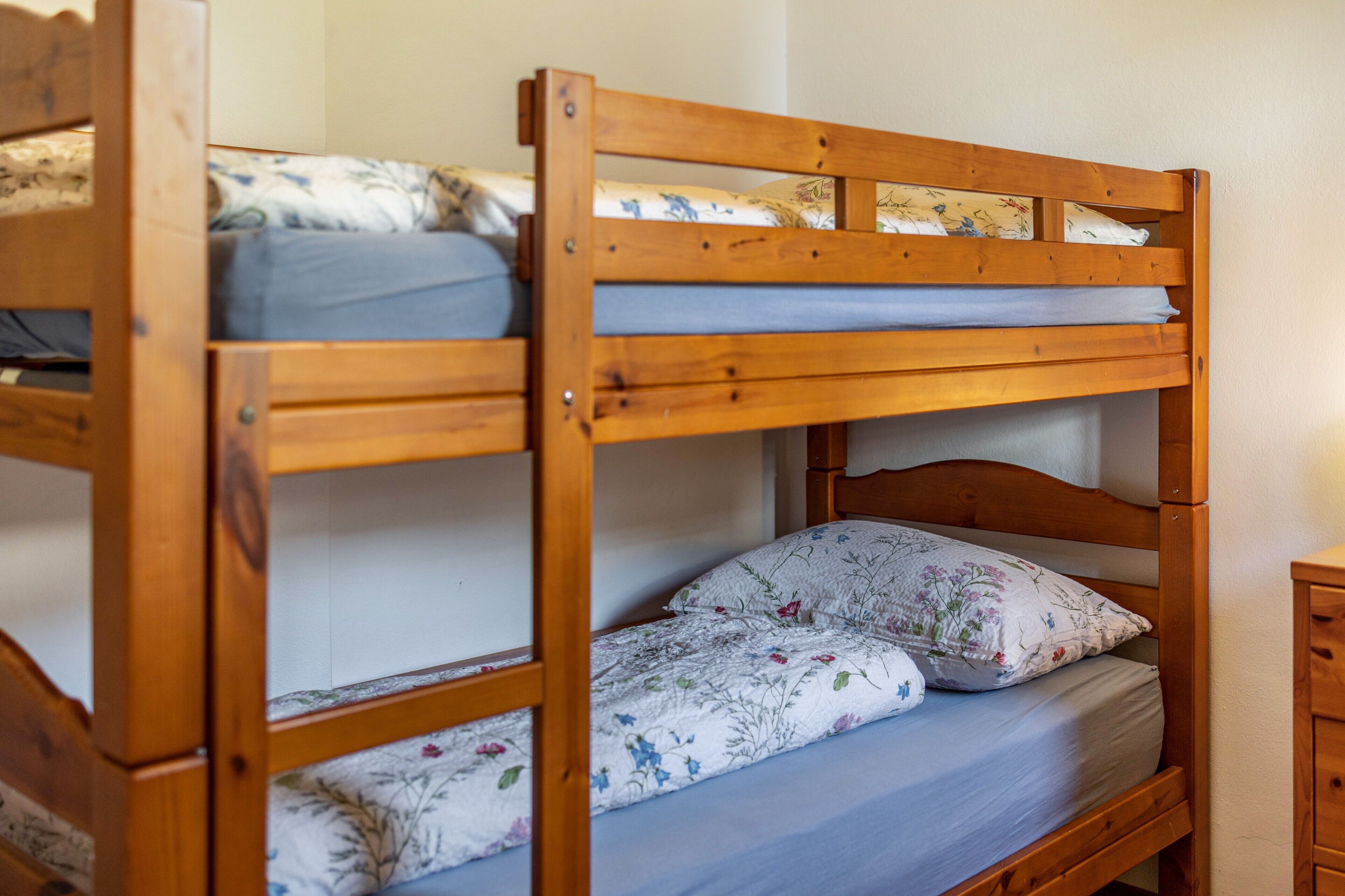 Ein Etagenbett mit Holzrahmen, das untere Bett mit einer blumengemusterten Matratze und das obere Bett mit einer schlichten Matratze.