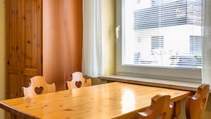 Une table à manger en bois, des chaises en forme de cœur, une fenêtre avec des stores et une porte en bois.