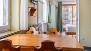 Une table de salle à manger en bois ornée de découpes en forme de cœur, un téléviseur fixé au mur et un lit avec un rideau vert.