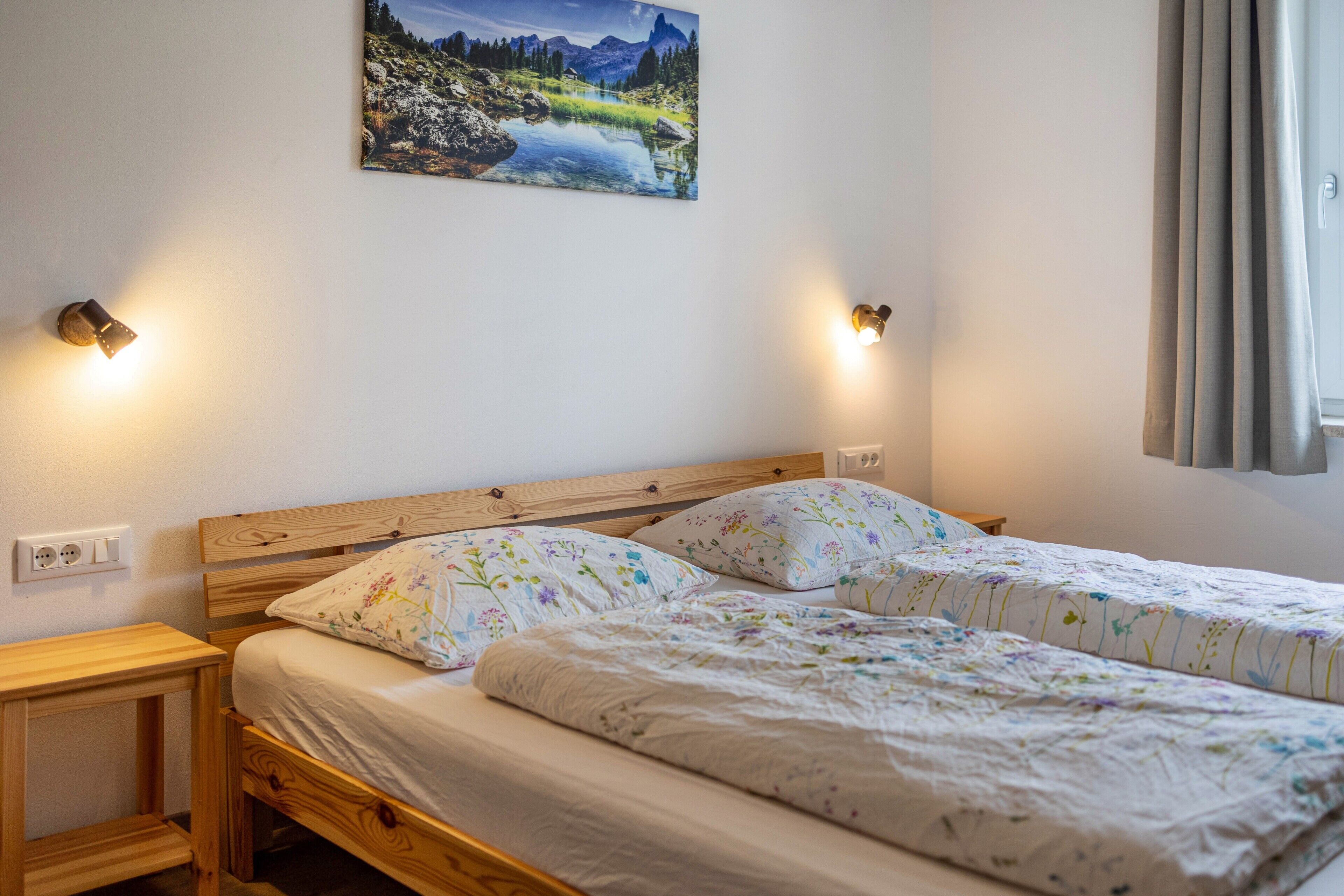 A bedroom with two beds, a wooden headboard, bedside lamps, a nightstand, and a painting on the wall.