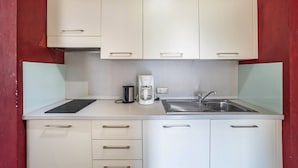 Cocina compacta con armarios blancos, cafetera y pileta.