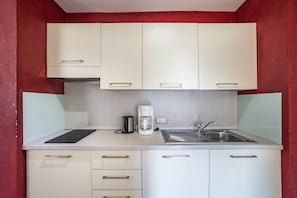 A compact kitchen with white cabinets, a coffee maker, and a sink.