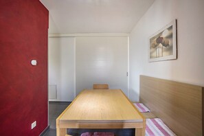 A room with a wooden table, a bed with a wooden headboard, a red wall, and a framed picture on the wall.