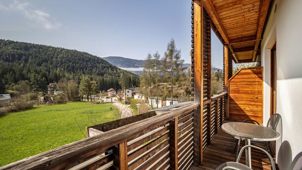 Un balcón de madera con una mesa y sillas, con vistas a un campo verde y colinas boscosas.