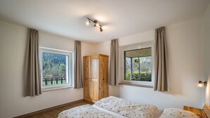 Ein Schlafzimmer mit zwei Betten, einem Holzschrank und großen Fenstern mit Vorhängen.