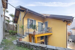 A yellow building with a balcony, potted plants, and a stone wall.