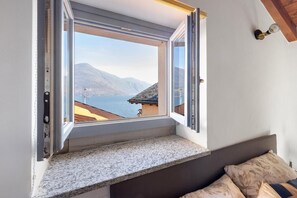 A room with a window overlooking a body of water and mountains, a bed with patterned pillows, and a granite countertop. - Apartment 'Casa Valy' with Lake View, Wi-Fi and Air Conditioning (Cannobio)