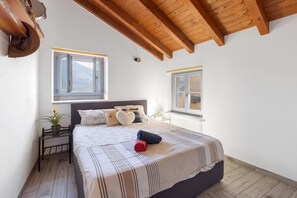 A bedroom with a bed, two windows, a radiator, and a wooden ceiling.