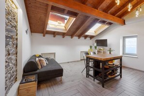 A loft-style room with a stone wall, a black sofa, a wooden dining table, and skylights.