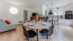 A modern kitchen with white cabinets, a microwave, and an oven. There is a dining area with a round table, chairs, and a pineapple centerpiece.