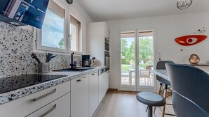 A modern kitchen with a granite countertop, white cabinets, a dining area with a table and chairs, and a view of the outdoors through a glass door.
