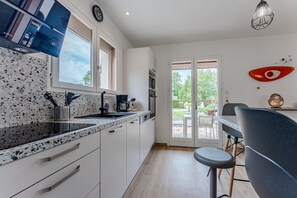 Une cuisine moderne dotée d’un comptoir en granit, de meubles blancs, d’un coin repas avec une table et des chaises, et offrant une vue sur l’extérieur grâce à une porte vitrée.