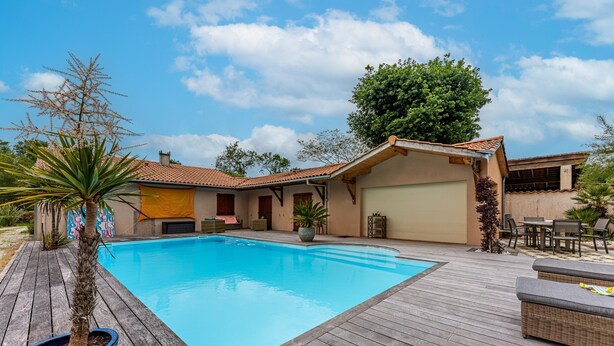 A swimming pool with a wooden deck, a covered patio area, and a garage.